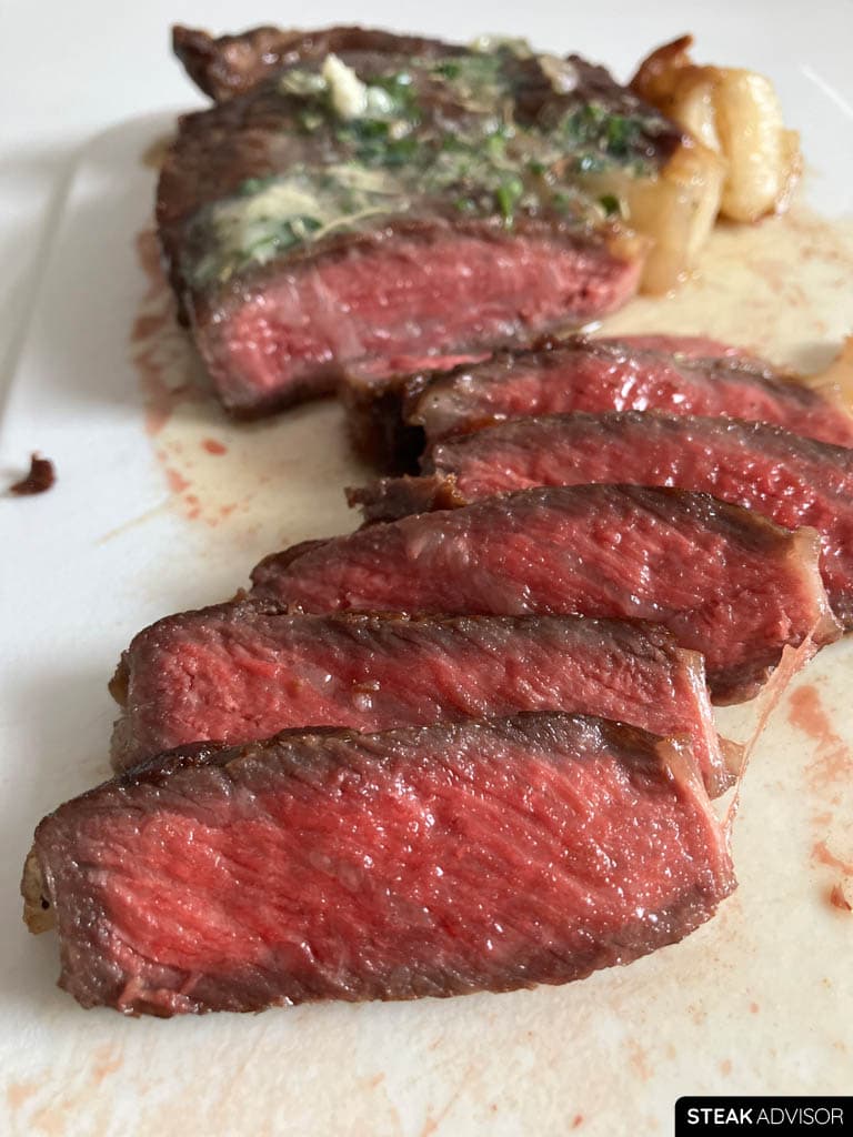Cast-iron-seared steak sliced and served on a white board with garlic butter on top