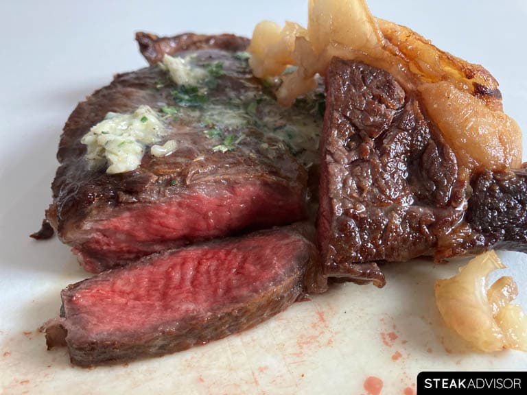 Steak cooked in a cast-iron skillet to medium-rare doneness, sliced and served with garlic butter on top.