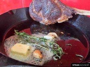 Cowboy steak seared in a cast iron skillet with butter, rosemary, and garlic.