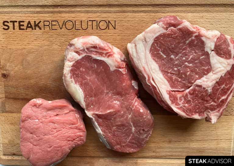 Filet mignon, New York strip, and ribeye on a wooden cutting board.
