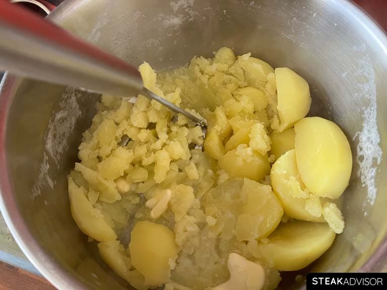 Mashing potatoes with milk and butter in a pot