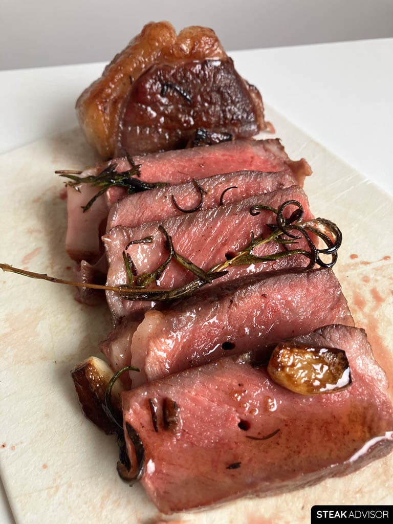 Reverse-seared steak served on a white cutting board with aromatics