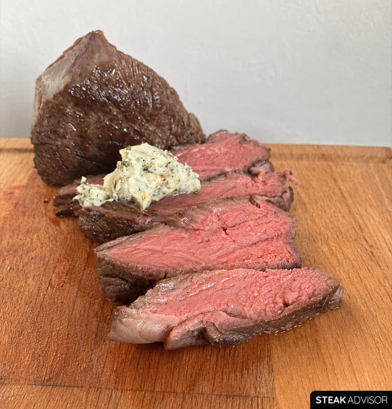 Sliced sous vide steak served with compound butter, seared garlic, and herbs.