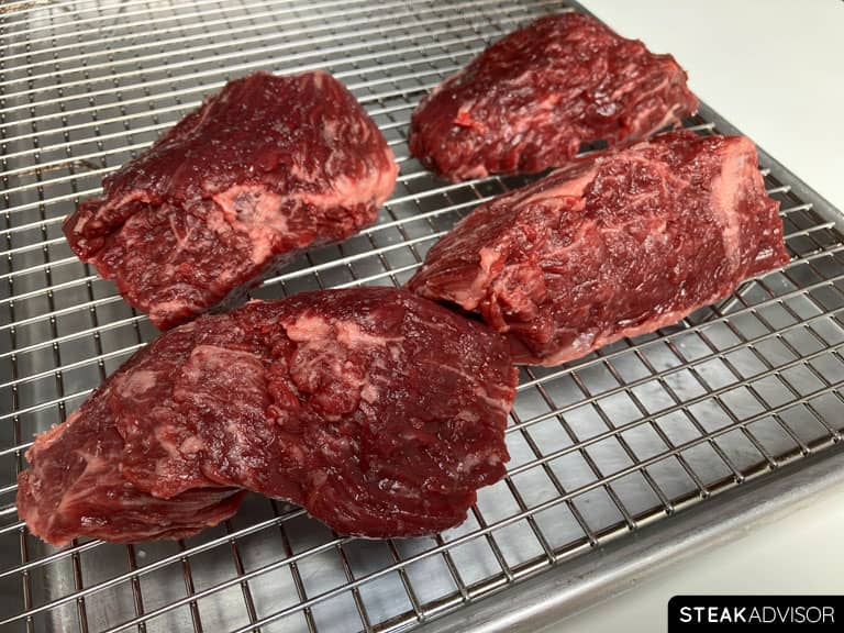 Salt-seasoned hanger steak pieces arranged on a wire rack over a baking sheet.