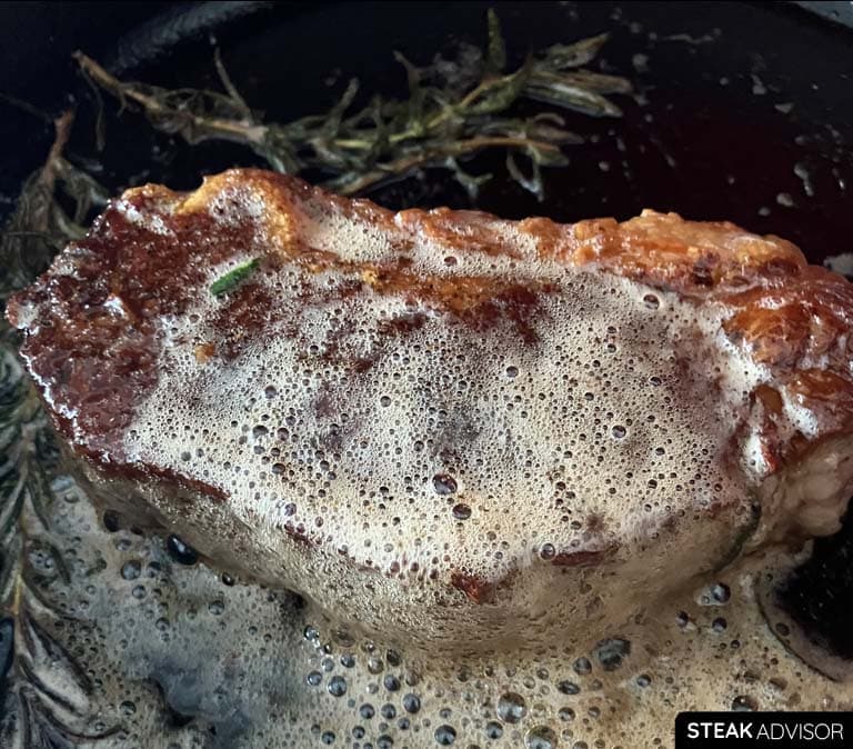 Steak being butter-basted in a pan with aromatics.