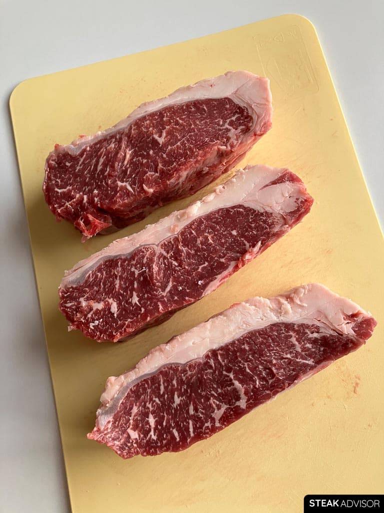 Three well-marbled strip steaks on a cutting board