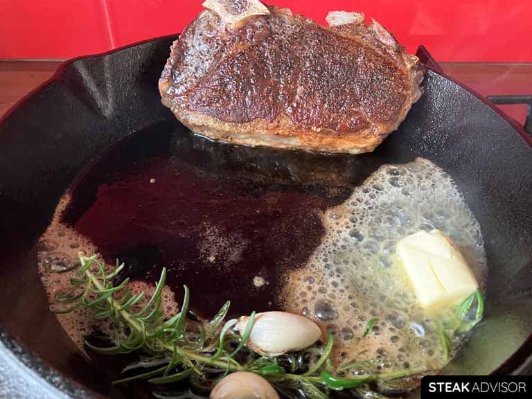 Bone in new york strip seared in a cast iron skillet with butter, rosemary, and garlic.