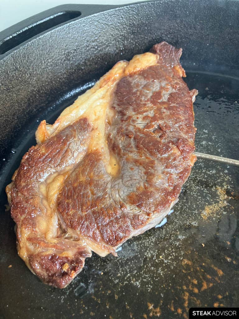 Steak seared in a cast-iron skillet with a golden-brown crust.
