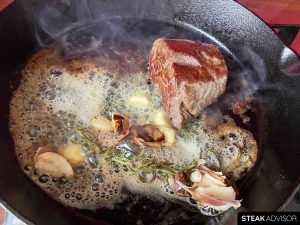 flat iron steak seared in a cast iron skillet with butter, rosemary, and garlic.
