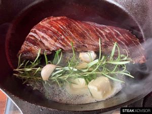 Hanger steak seared in a cast iron skillet with butter, rosemary, and garlic.