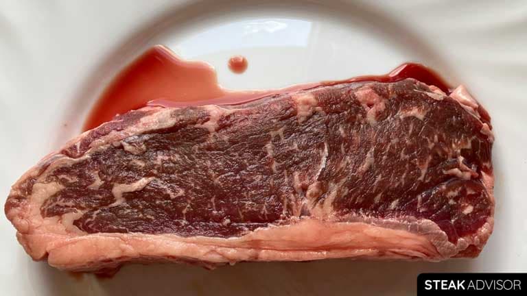 Raw strip steak with red juice on plate