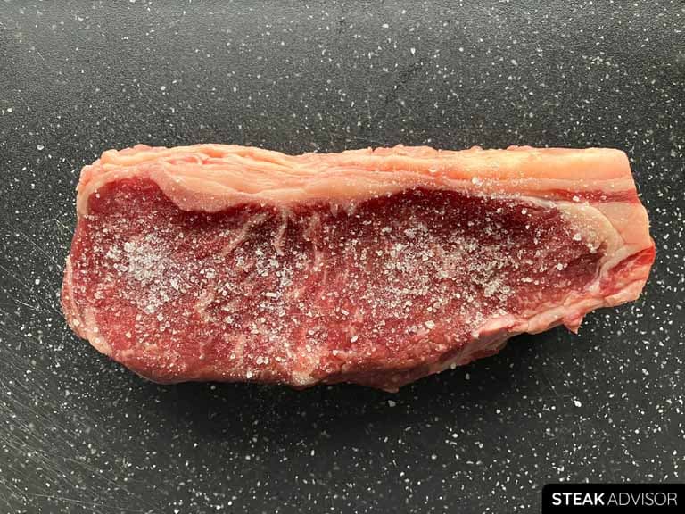 Strip steak seasoned with salt on a black cutting board