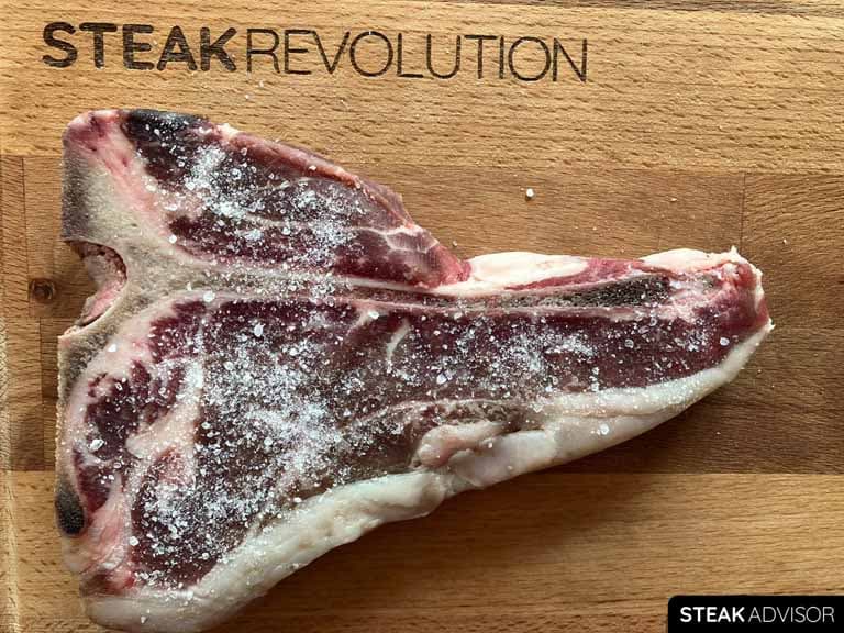 salt seasoned t-bone steak on a steak revolution wood cutting board