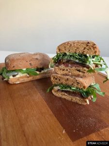 Skirt steak sandwiches, served on a wooden cutting board.