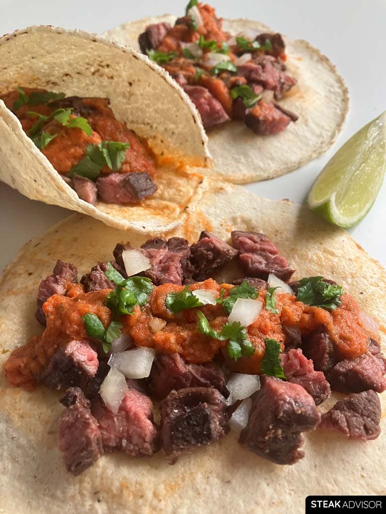 Skirt steak tacos topped with salsa roja, diced onions, cilantro, and lime juice