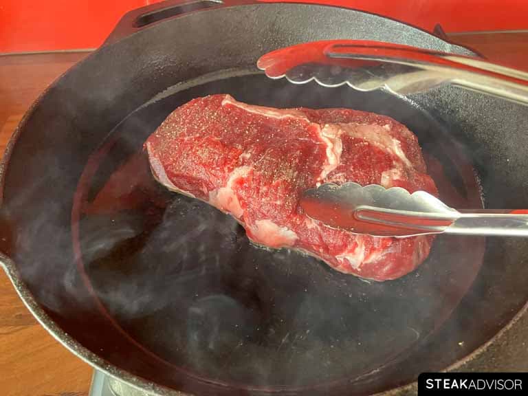 steak pressed with tongs in a hot pan.
