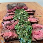 Steak served with chimichurri on a wooden cutting board