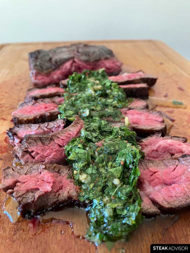 Steak served with chimichurri on a wooden cutting board
