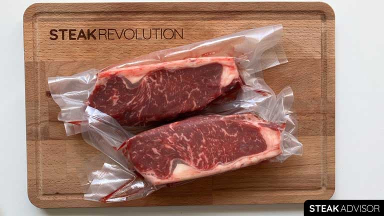 Two vacuum-packed strip steaks on a wood-cutting board